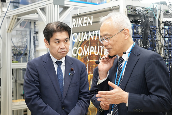 超伝導量子コンピュータ「叡」の前で説明を受けられる松本 大臣の写真